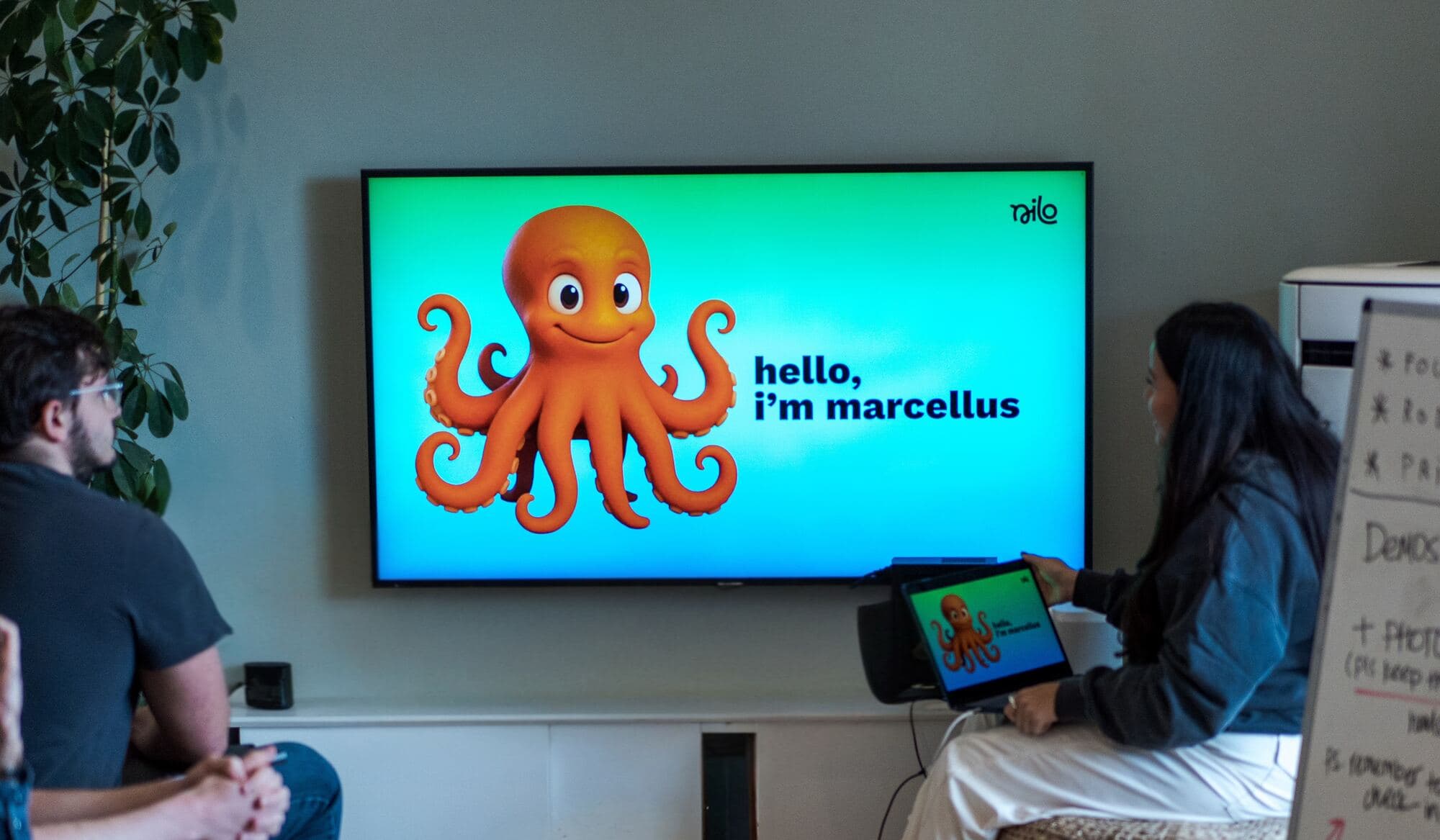 Nilo team gathered around a TV with a character named Marcellus on screen during the Marcellus offsite.